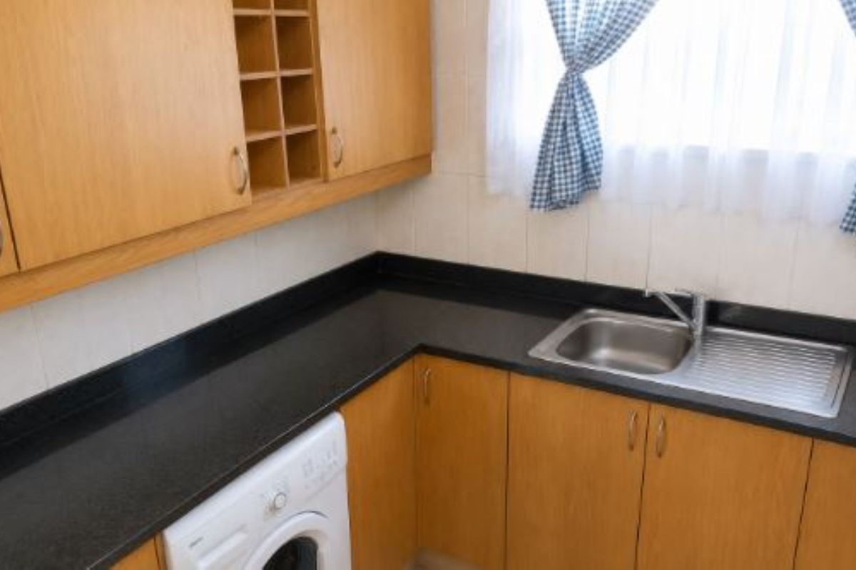 A functional kitchen area featuring light wood-tone cabinetry, black countertops, a stainless steel sink, and a tiled splashback.