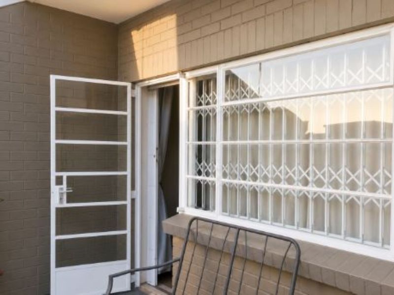 A covered patio area featuring painted brick walls, a white security gate, and windows fitted with protective security bars.