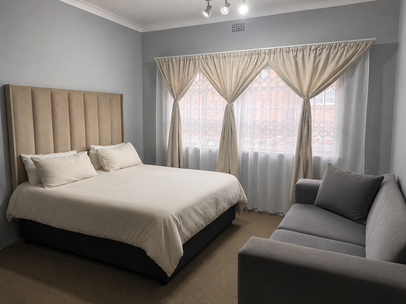 A well-maintained bedroom featuring neutral wall tones, carpeted flooring, and a window fitted with a security gate.