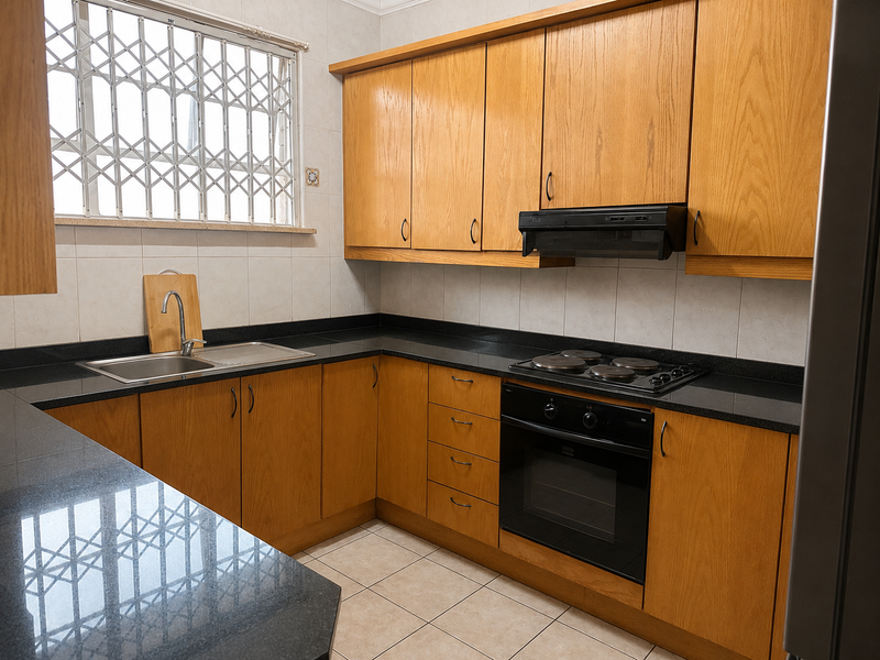 A functional kitchen featuring wooden cabinetry, granite countertops, a built-in oven with electric hob, and a window with security gate.