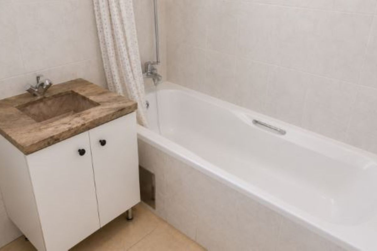 A functional bathroom featuring a white vanity cabinet with an integrated sink, a standard bathtub with shower mixer, and neutral wall tiling.