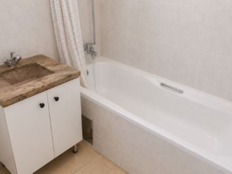 A functional bathroom featuring a white vanity cabinet with an integrated sink, a standard bathtub with shower mixer, and neutral wall tiling.