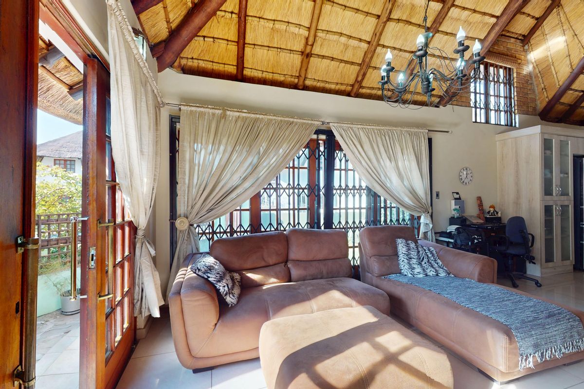 Spacious living area featuring a high vaulted thatched ceiling with exposed timber beams, tiled flooring, and direct access to the outdoor patio.