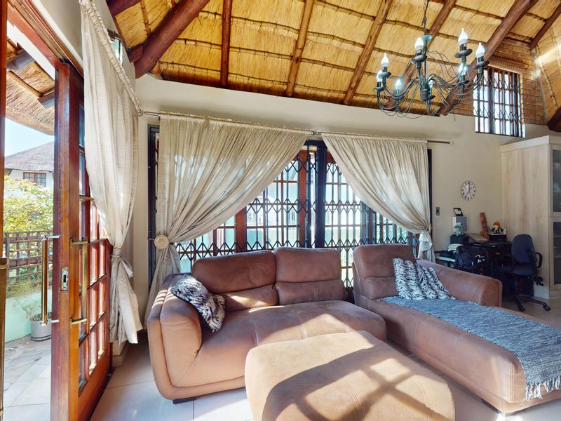 Spacious living area featuring a high vaulted thatched ceiling with exposed timber beams, tiled flooring, and direct access to the outdoor patio.