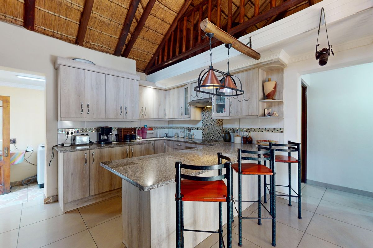A well-appointed kitchen featuring granite countertops, light wood-finish cabinetry, a tiled backsplash, and a distinctive high-pitched exposed thatch roof with timber trusses.