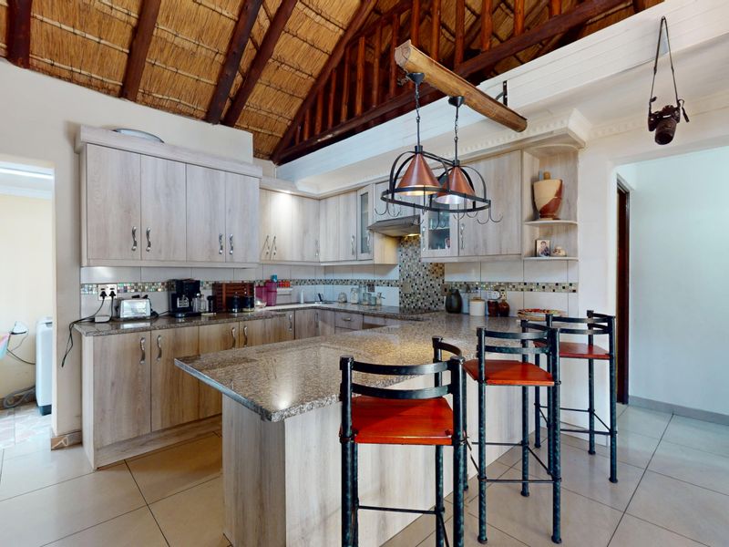 A well-appointed kitchen featuring granite countertops, light wood-finish cabinetry, a tiled backsplash, and a distinctive high-pitched exposed thatch roof with timber trusses.