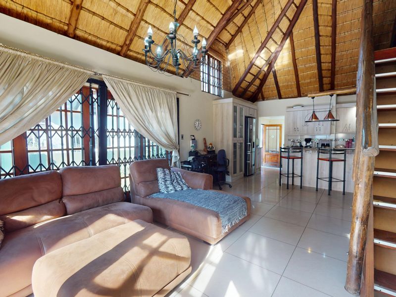 Spacious open-plan living area featuring a high thatched ceiling with exposed rafters, tiled flooring, a functional kitchen with breakfast bar, and a timber staircase.