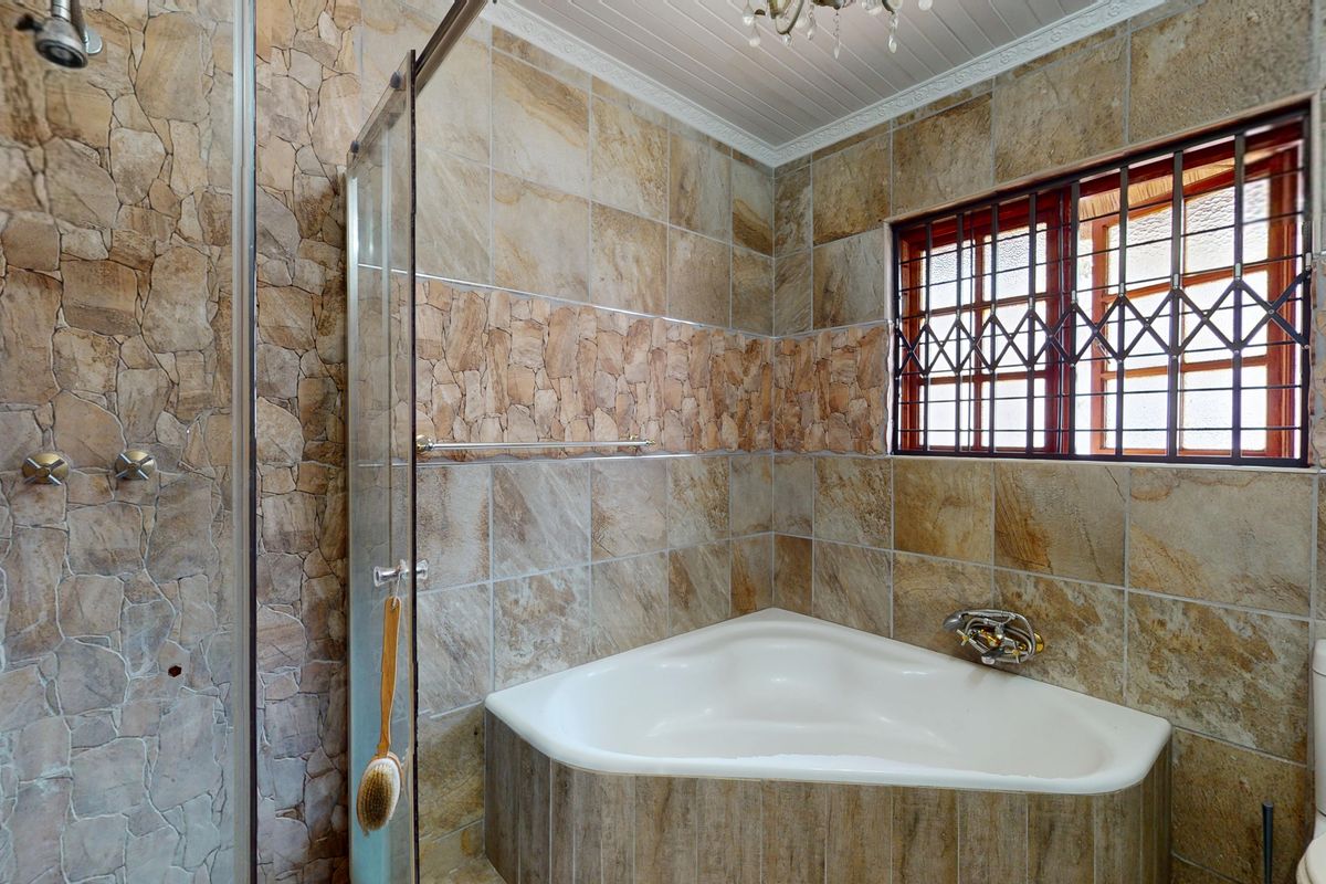 Bathroom featuring a corner bathtub, glass-enclosed shower, and textured stone wall tiling with security-barred window.
