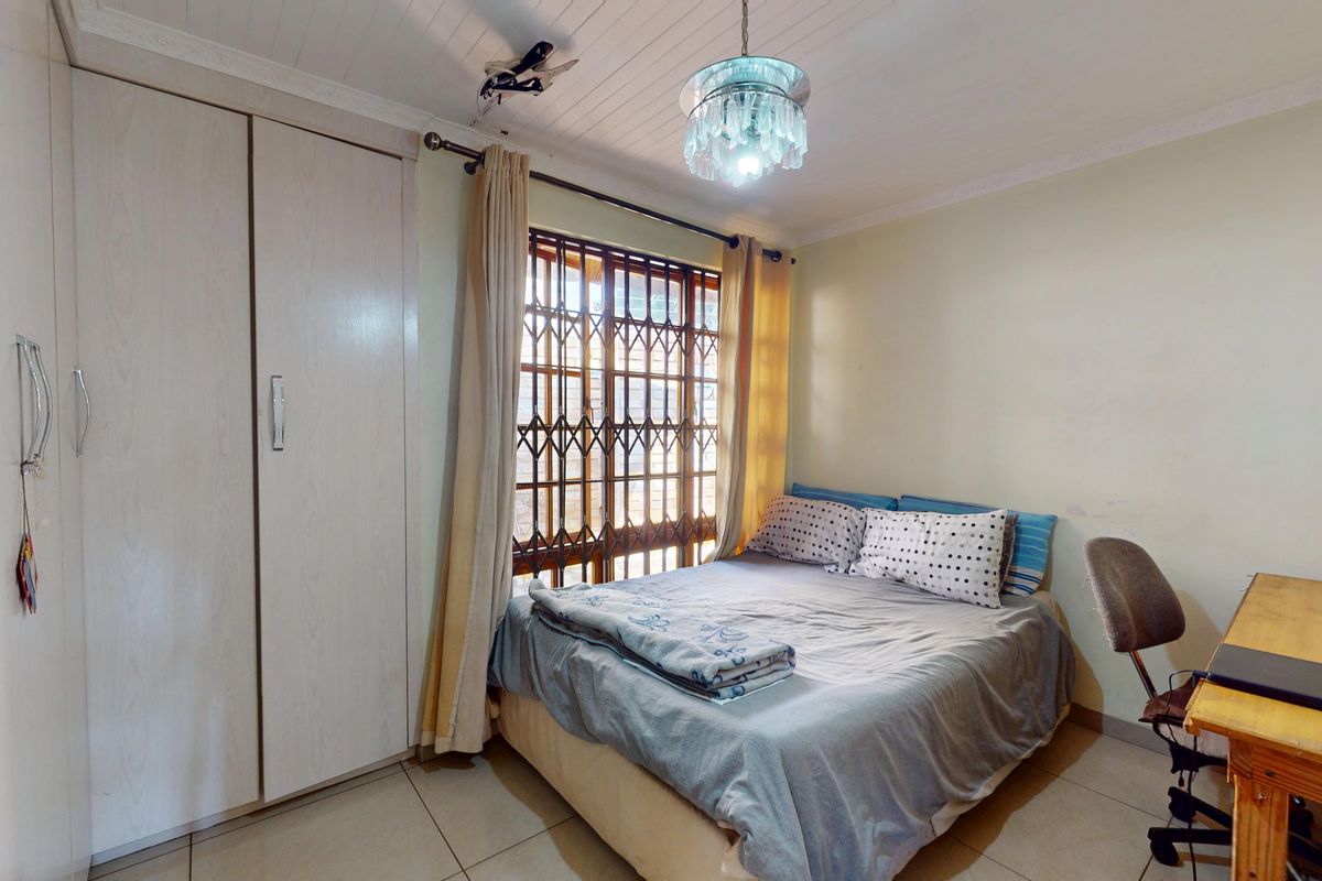A functional bedroom featuring built-in wardrobes, tiled flooring, and a security gate on the window, providing a practical and secure living space.