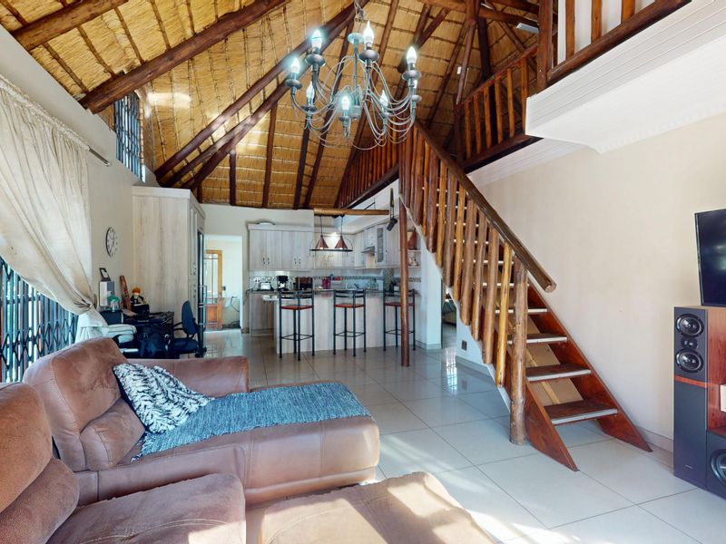 Open-plan living area featuring a high thatched ceiling with exposed timber trusses, a wooden staircase, and an integrated kitchen with island seating.