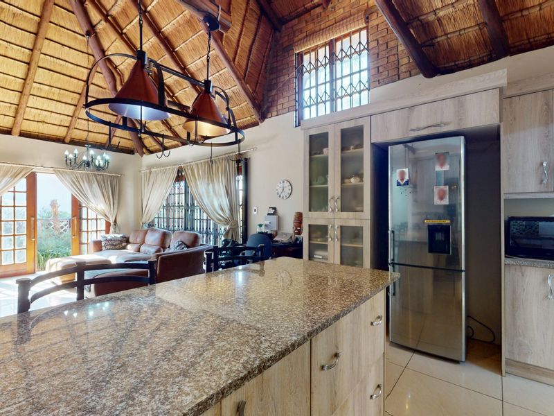 Spacious open-plan living area featuring a high vaulted thatch ceiling with exposed timber beams, a granite-topped kitchen island, and direct access to the patio.