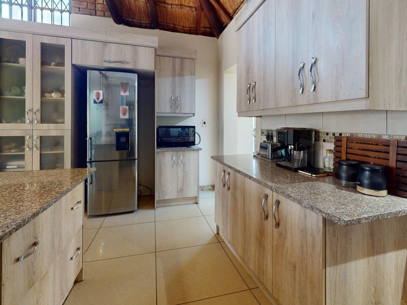 A well-appointed kitchen featuring granite countertops, light wood-finish cabinetry, tiled flooring, and a distinctive high-pitched thatch roof ceiling.