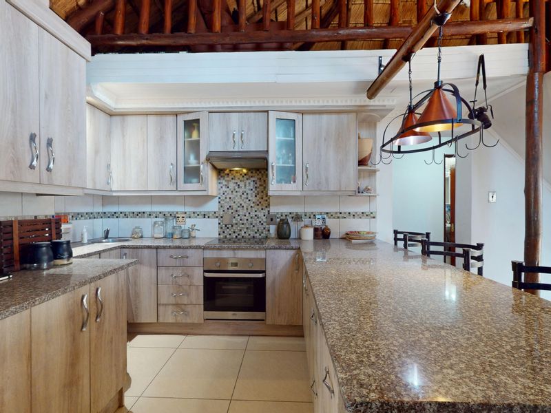 A well-appointed kitchen featuring light wood-grain cabinetry, granite countertops, mosaic backsplash, and a unique exposed timber roof structure.