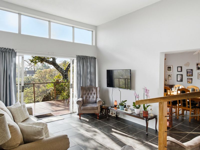 Bright living room featuring large sliding doors opening onto a timber deck, high ceilings with clerestory windows, and tiled flooring throughout.
