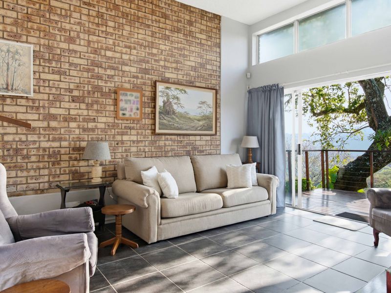 Bright living room featuring an exposed brick wall, large tiled floors, and sliding glass doors that open onto a balcony with scenic views.