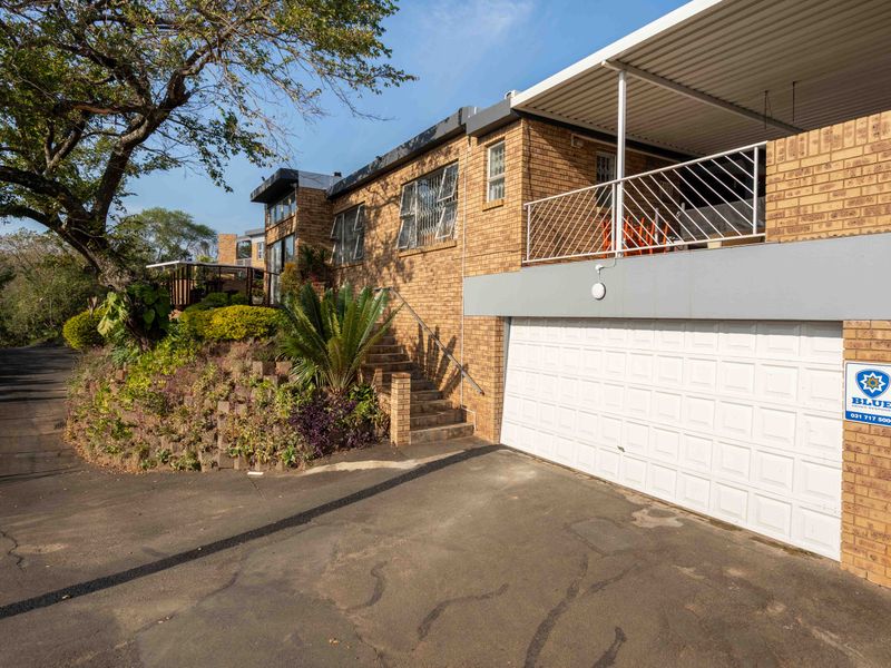 Front exterior view of a face brick townhouse featuring a garage, covered balcony, and paved driveway with established garden landscaping.