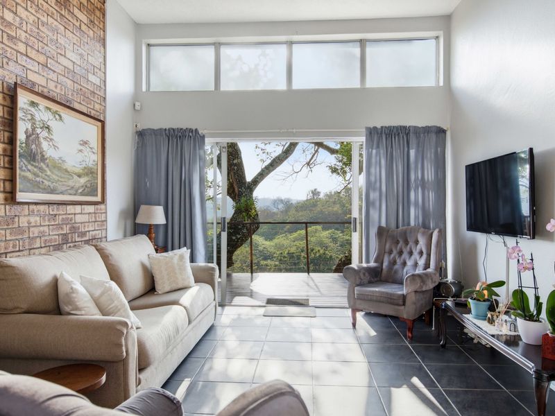 Bright living room featuring an exposed brick wall, high clerestory windows, and sliding glass doors opening onto a balcony with scenic views.