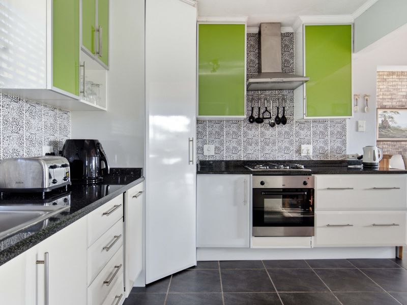Modern kitchen featuring high-gloss green and white cabinetry, granite countertops, stainless steel appliances, and a distinctive patterned tile backsplash.