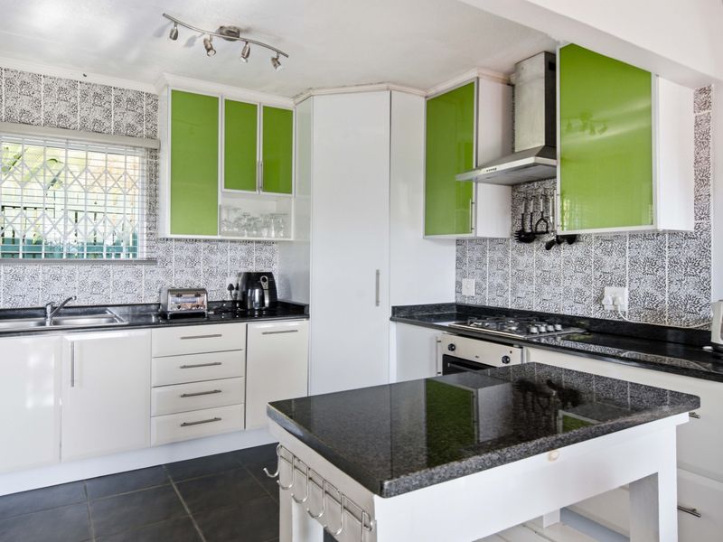 Modern kitchen featuring vibrant green and white cabinetry, granite countertops, built-in gas hob, oven, and extractor fan with tiled flooring.