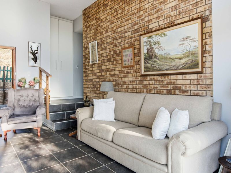 Living room featuring a prominent exposed brick wall, dark tiled flooring, and a staircase leading to an elevated storage area.