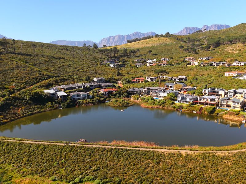 An aerial view of a residential estate situated around a lake, featuring scenic mountain views and landscaped surroundings.