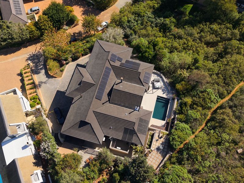 Aerial view of a residential property featuring a dark tiled roof with integrated solar panels, a swimming pool, and surrounding landscaped garden areas.