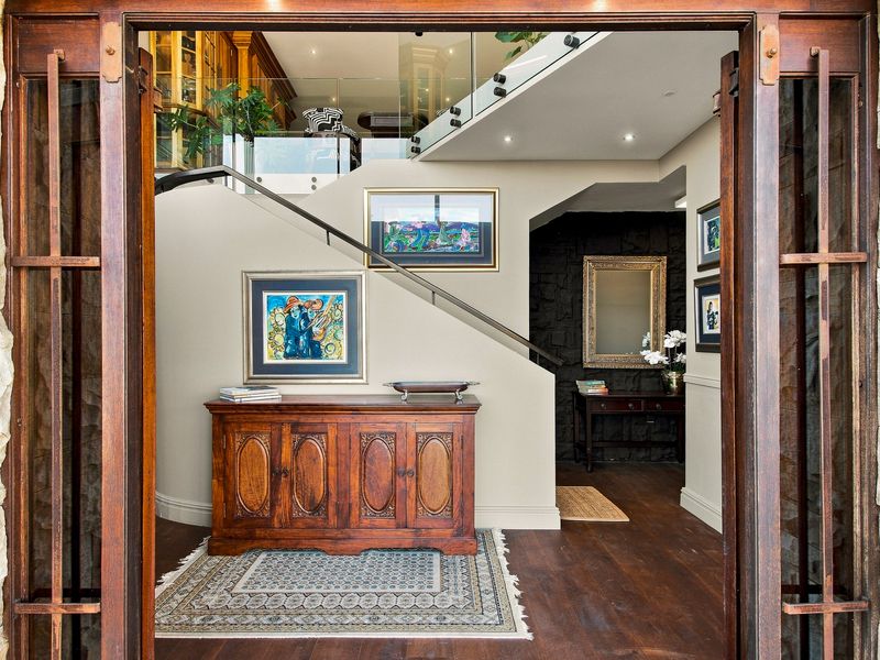 Elegant entrance foyer featuring hardwood flooring, stone-clad exterior framing, and a modern staircase with a glass balustrade.