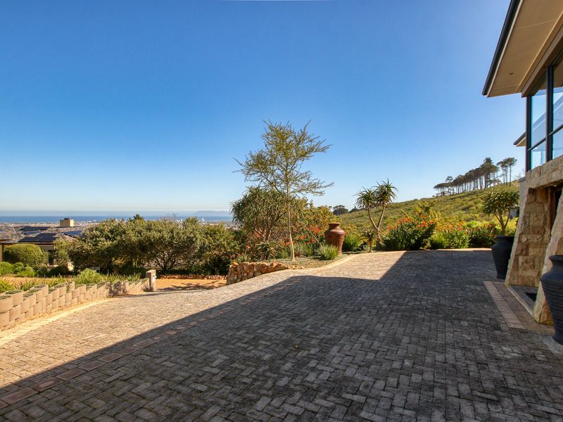 A well-maintained paved driveway leading to a stone-clad home, featuring landscaped gardens and expansive coastal views.