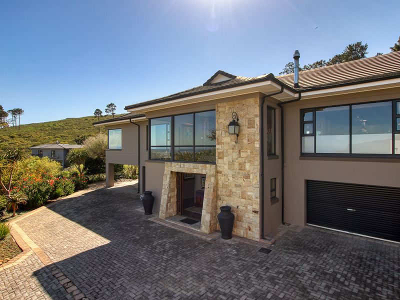 A well-maintained modern residence featuring stone cladding, a paved driveway, and a secure garage, set against a scenic hillside backdrop.