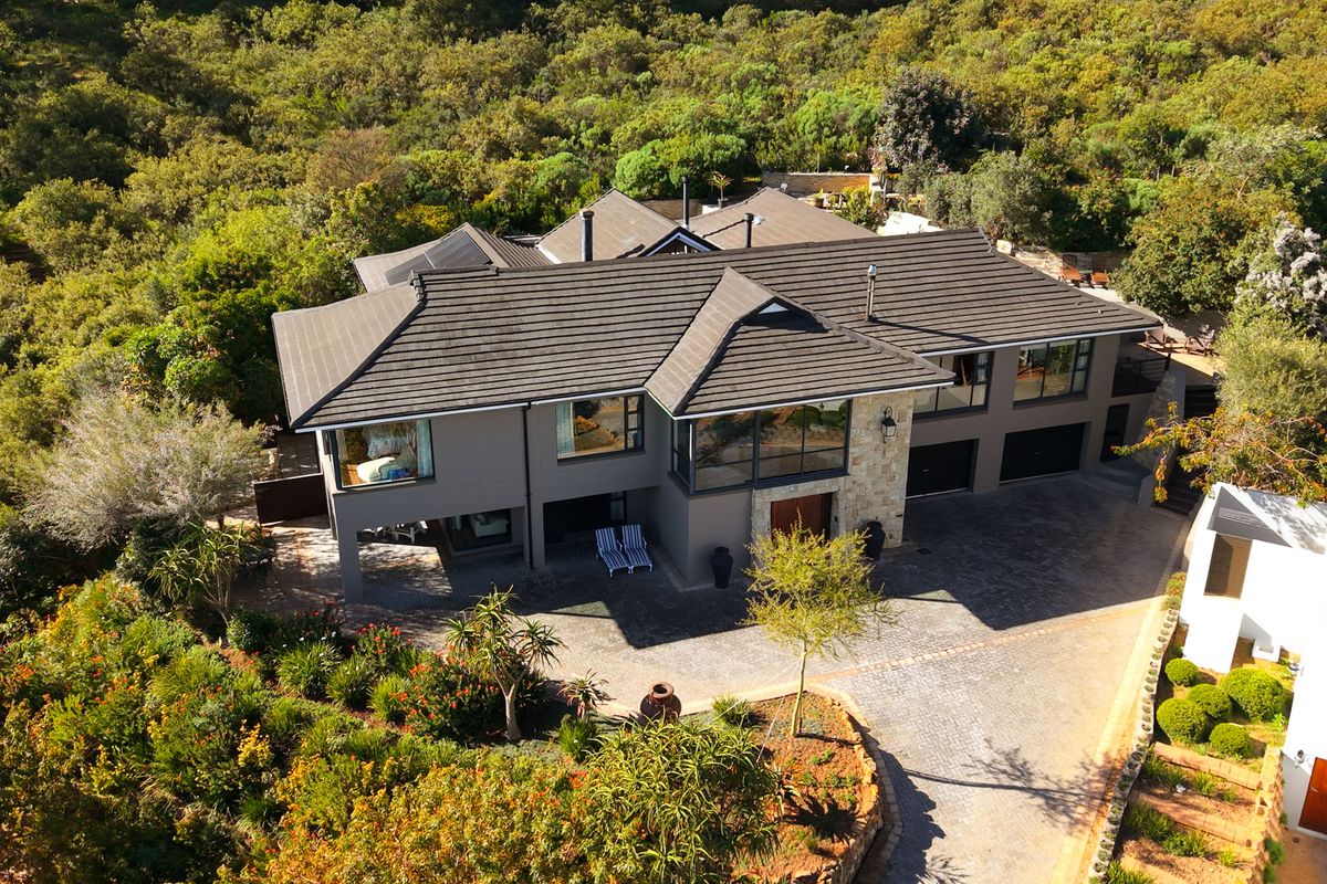 Aerial view of a modern multi-level residence featuring a tiled roof, stone facade accents, and a spacious paved driveway set within a lush landscape.