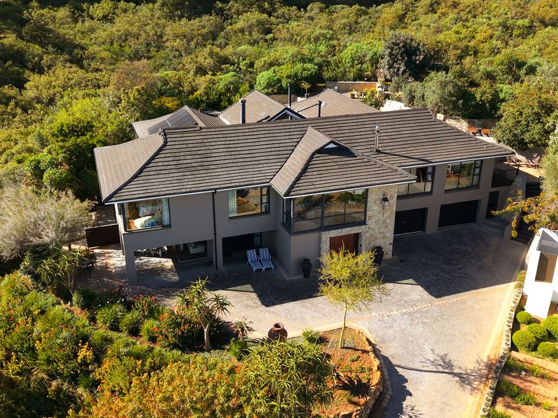 Aerial view of a modern multi-level residence featuring a tiled roof, stone facade accents, and a spacious paved driveway set within a lush landscape.