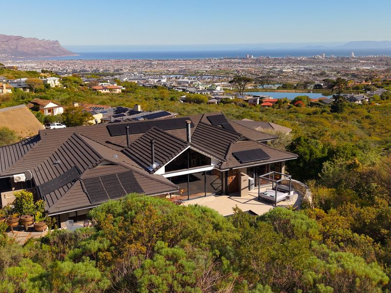 Aerial view of a modern house with a tiled roof, solar panels, and a spacious patio overlooking a scenic coastal landscape.