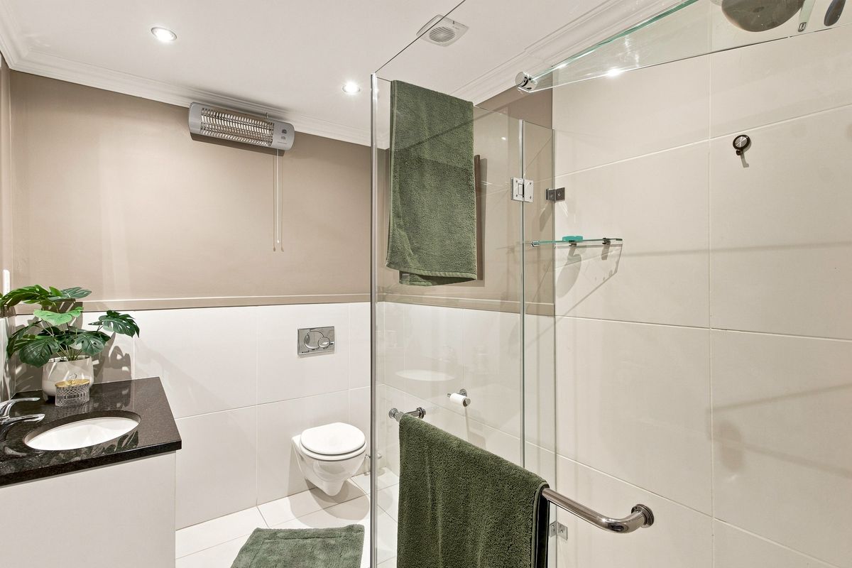 Modern bathroom featuring a glass-enclosed shower, wall-mounted toilet, and a vanity with a stone countertop, finished with clean tiling and recessed lighting.
