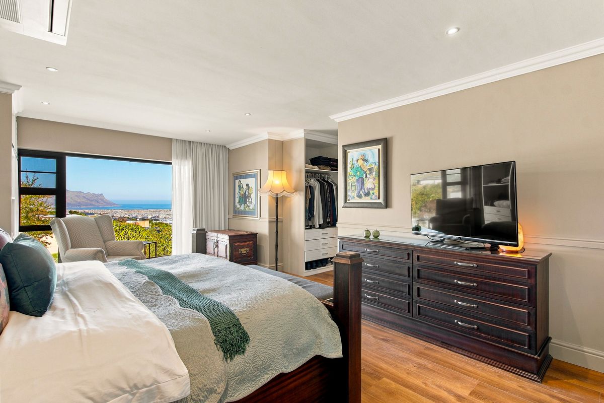 Spacious bedroom featuring hardwood flooring, crown molding, built-in wardrobe, and a large sliding glass door offering panoramic coastal and mountain views.