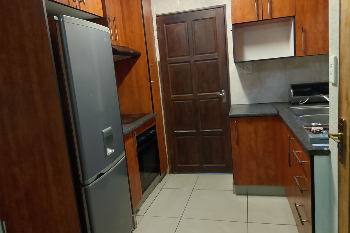 A functional kitchen featuring wood-finish cabinetry, laminate countertops, a built-in oven with hob, and tiled flooring with direct access to an exterior door.