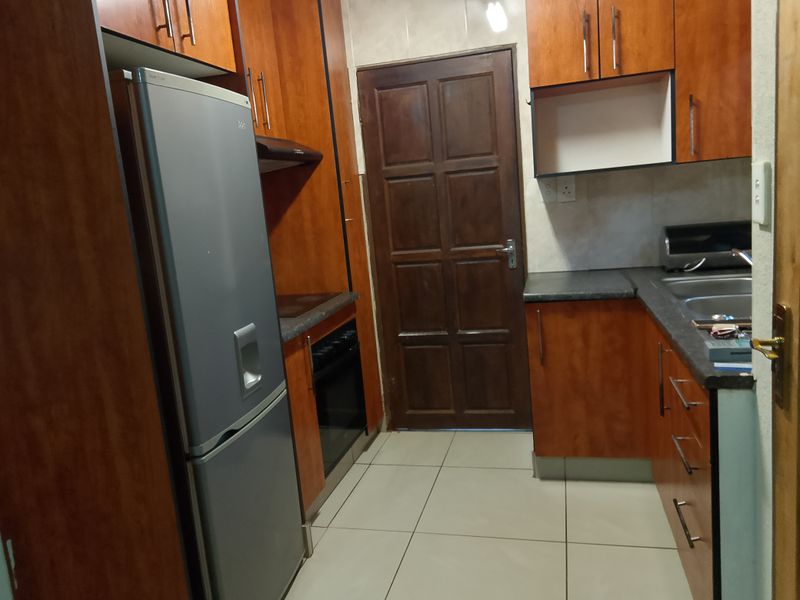 A functional kitchen featuring wood-finish cabinetry, laminate countertops, a built-in oven with hob, and tiled flooring with direct access to an exterior door.
