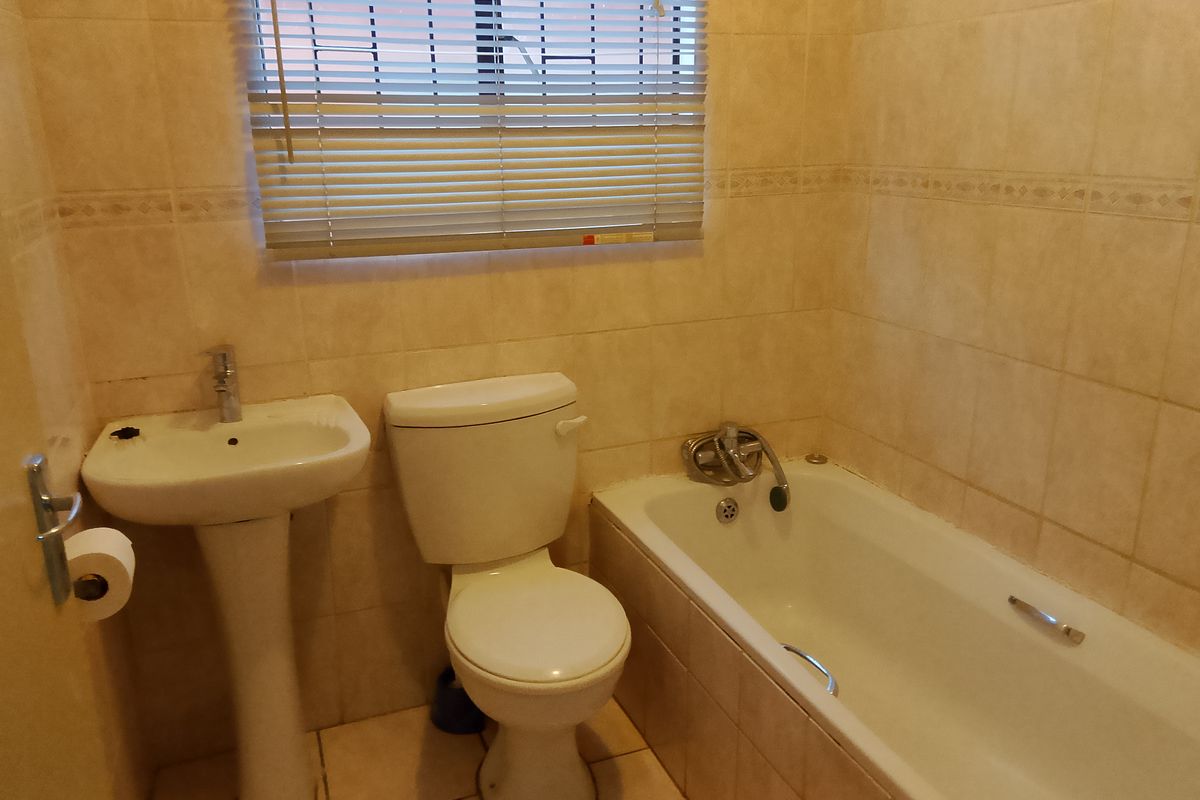 A functional bathroom featuring a pedestal basin, toilet, and bathtub with full-height wall tiling and neutral floor tiles.