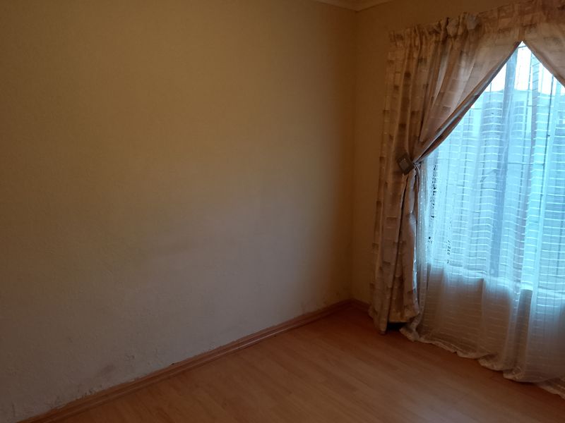 An empty bedroom featuring laminate flooring and visible wall surface wear, requiring cosmetic attention.