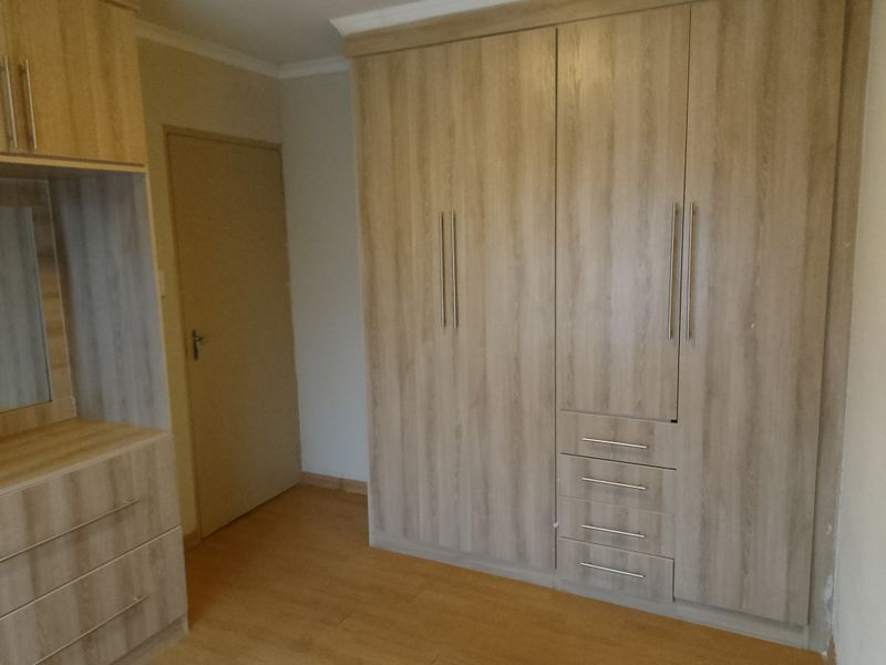 A clean bedroom featuring modern light wood-finish built-in cupboards, a matching vanity unit, and laminate flooring.