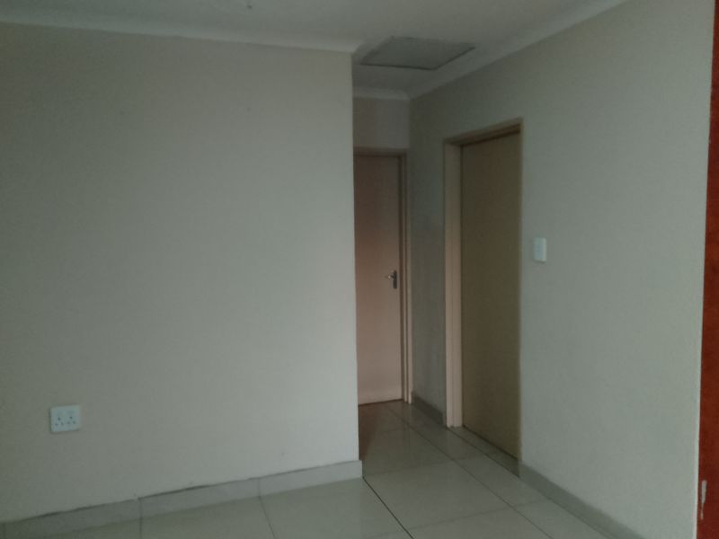 A neutral, empty hallway featuring tiled flooring and access to multiple internal rooms.