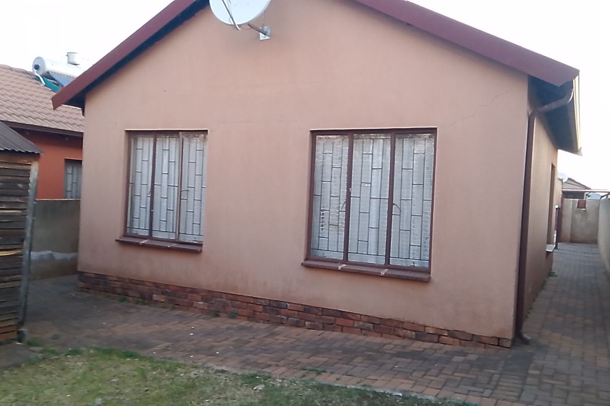 Rear exterior view of the house featuring brick paving, security bars on windows, and a satellite dish mounted on the roof.