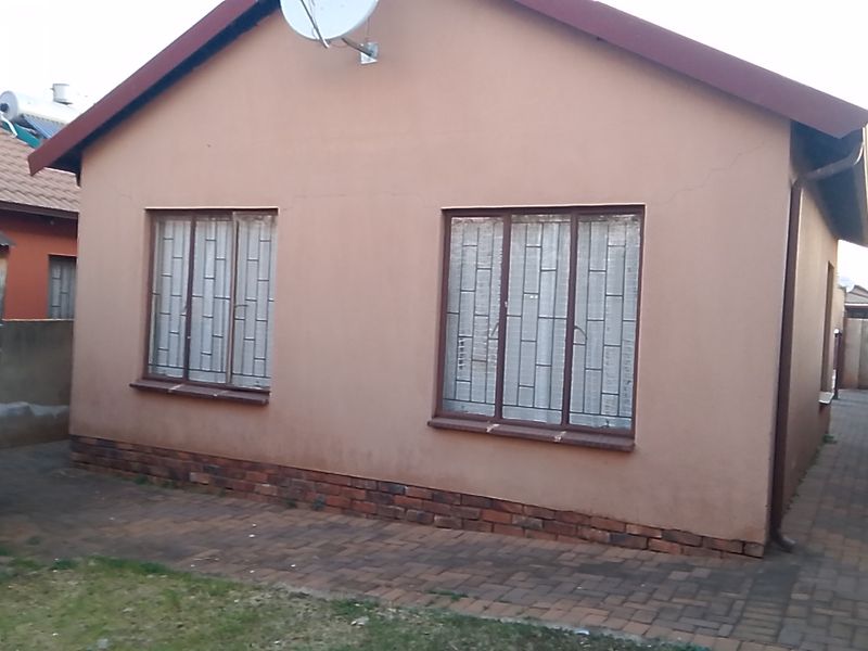 Rear exterior view of the house featuring brick paving, security bars on windows, and a satellite dish mounted on the roof.