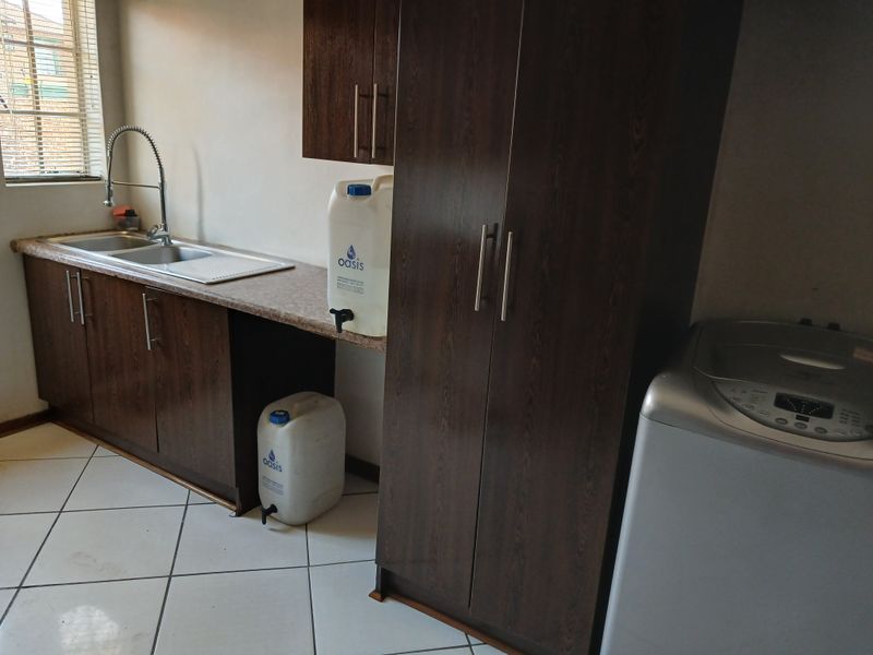 A functional laundry area featuring dark wood-finish cabinetry, a stainless steel sink with a modern faucet, and tiled flooring.