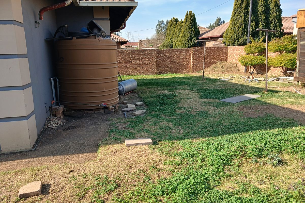 Rear garden area featuring a water storage tank, brick boundary wall, and tiled roof overhang.