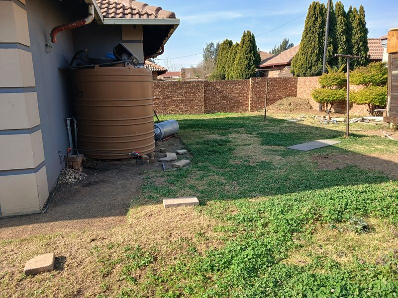 Rear garden area featuring a water storage tank, brick boundary wall, and tiled roof overhang.