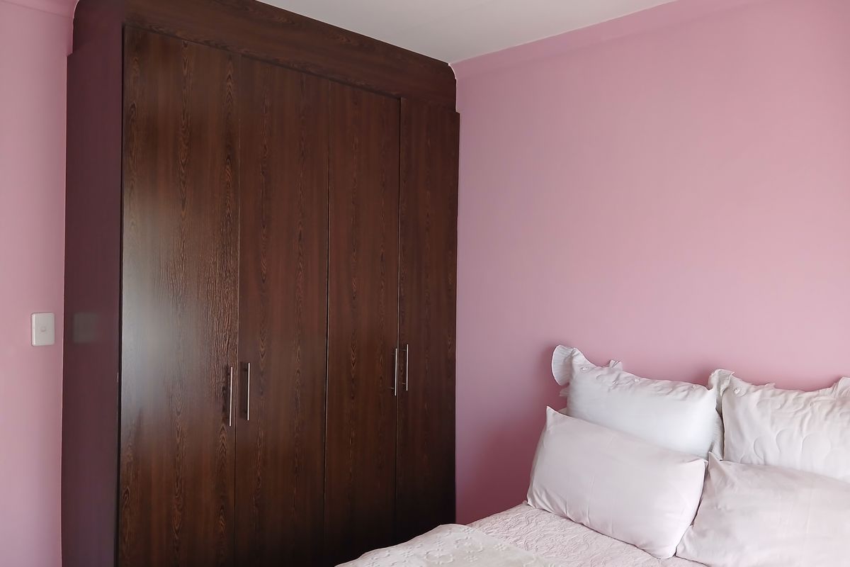 A bedroom featuring a dark wood-finish built-in wardrobe and pink painted walls.