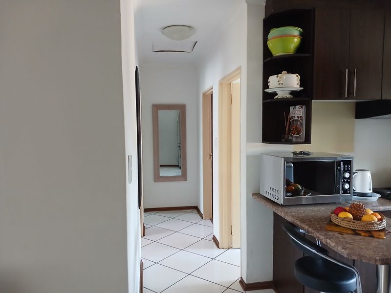A functional kitchen area featuring dark wood cabinetry and laminate countertops, leading into a tiled hallway with access to internal rooms.