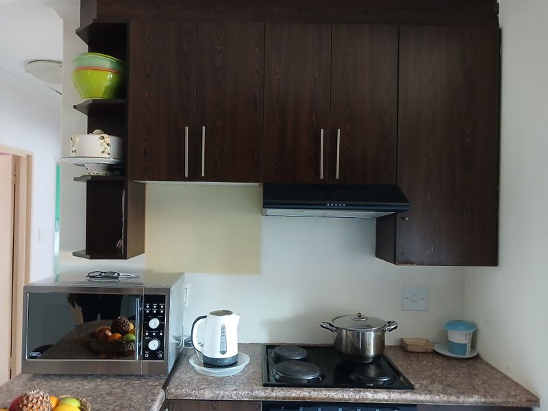 Kitchen area featuring dark wood cabinetry, laminate countertops, an electric hob with extractor fan, and a built-in microwave.