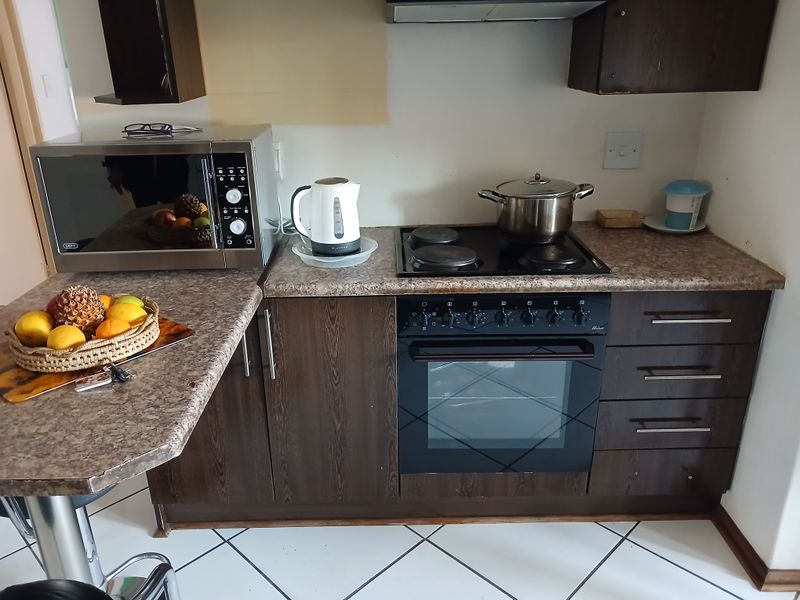 A functional kitchen area featuring dark wood cabinetry, laminate countertops, a built-in oven with an electric hob, and an extractor fan.