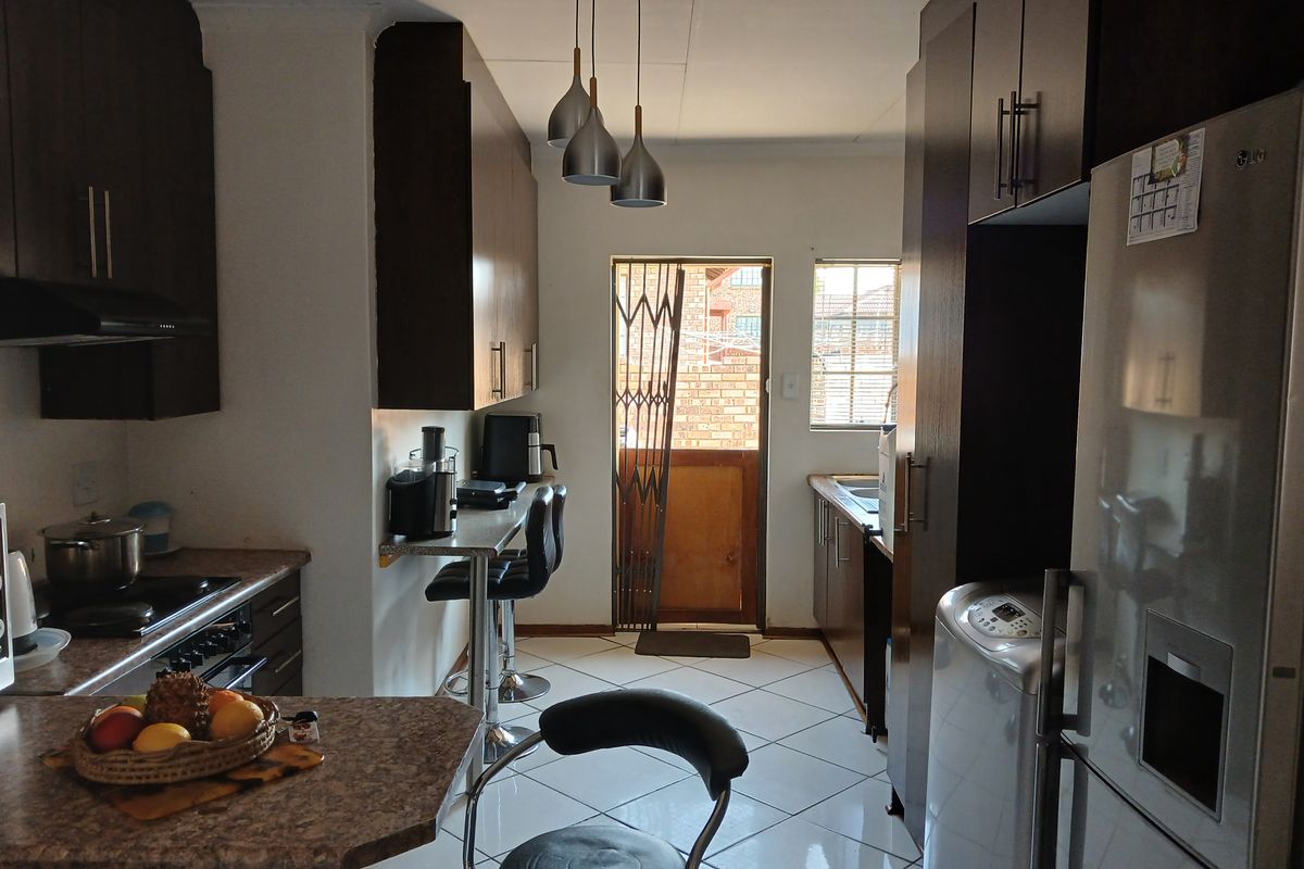 A functional kitchen featuring dark cabinetry, laminate countertops, tiled flooring, and direct access to the exterior via a security gate.